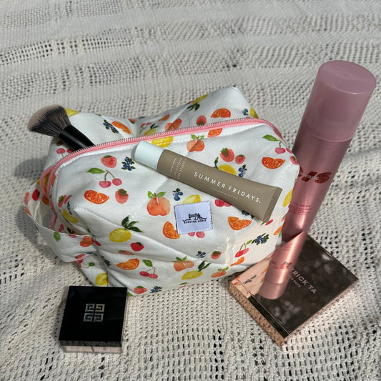 Makeup bag with cosmetic items including a brush, tube, and bottle on a textured surface.