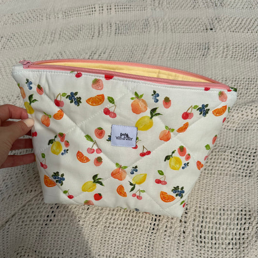 Small pouch with fruit pattern held on a textured fabric background
